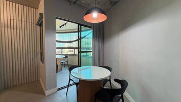 A modern interior with a round table, black chairs, a hanging pendant light, and a view through large windows.
