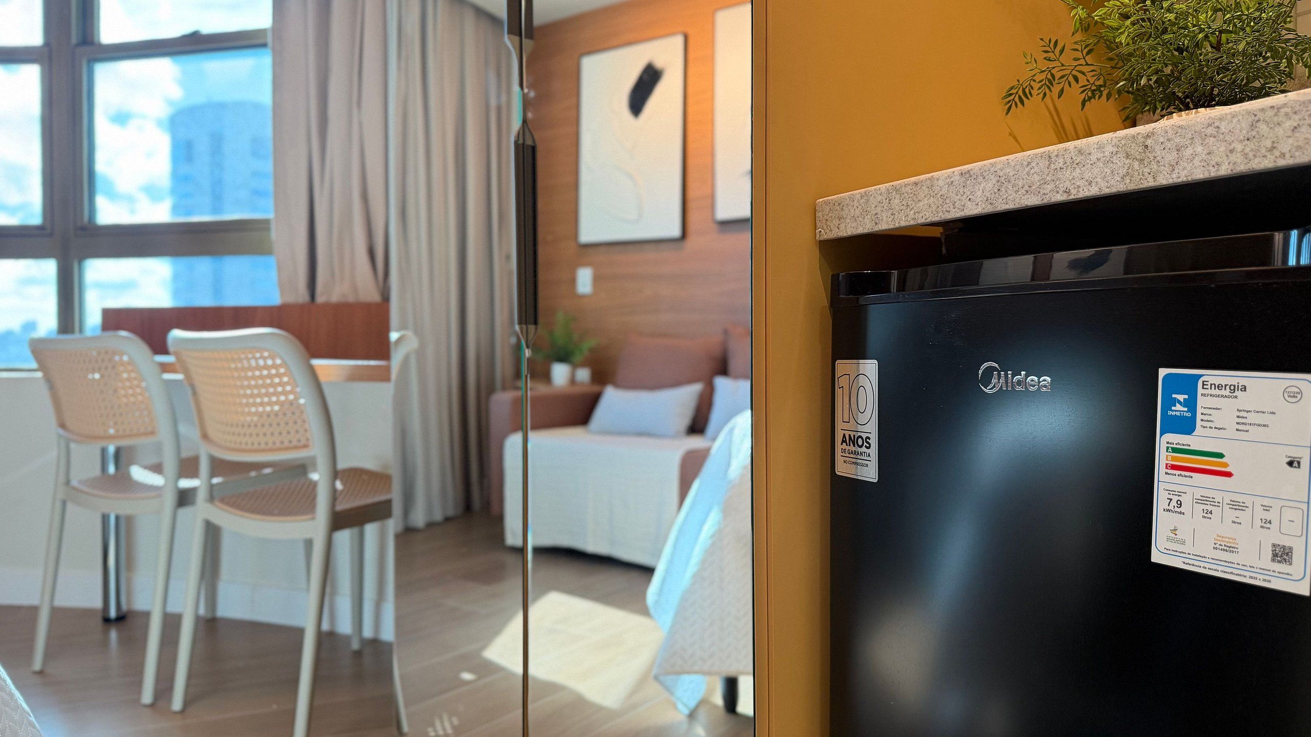 Una habitación de hotel moderna con comedor, una cama y un refrigerador negro con una pegatina.