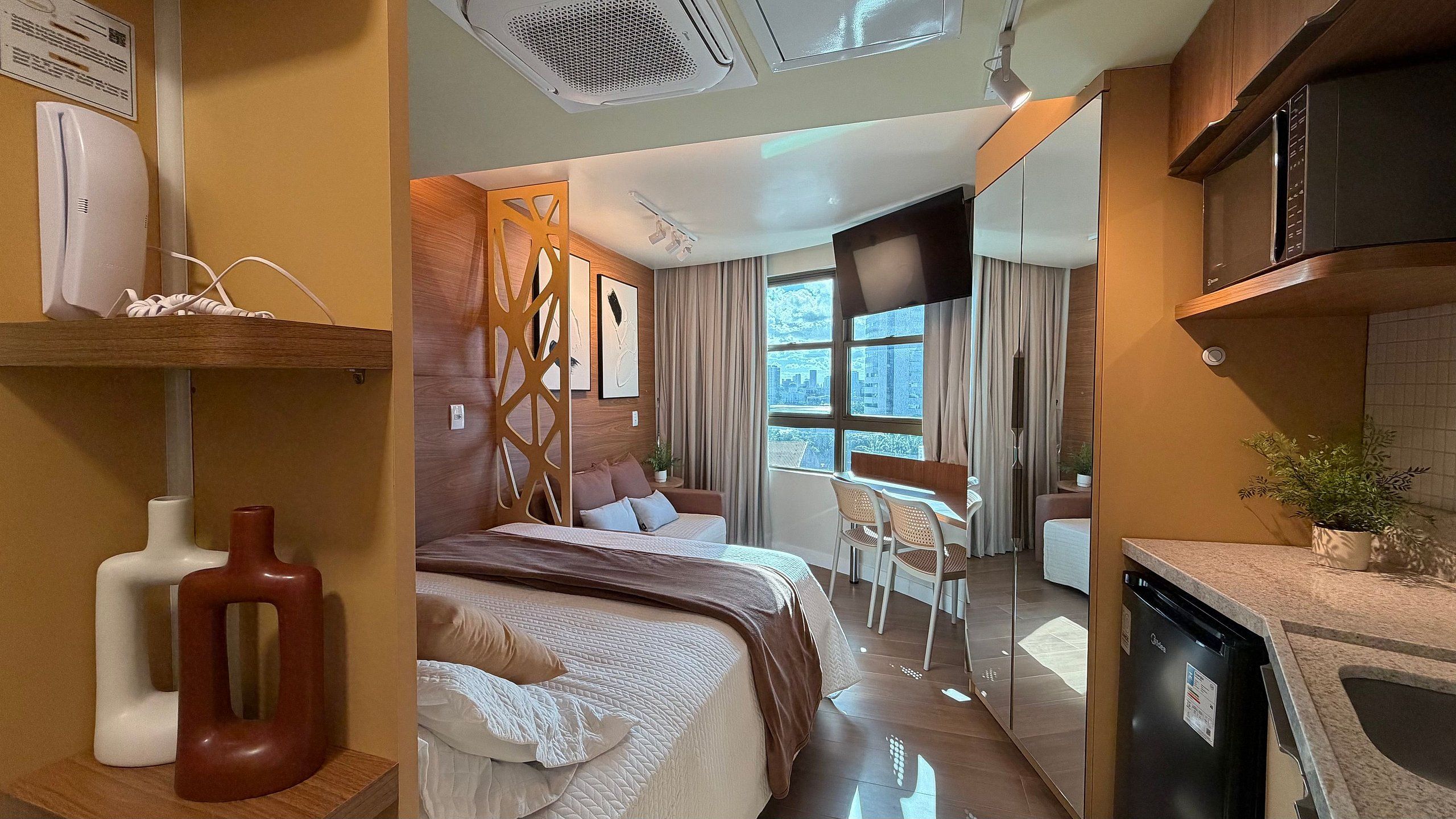 A modern hotel room with a bed, a dining area, and a kitchen.