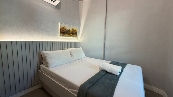 A single bed with white bedding, a grey headboard, and a framed picture on the wall.