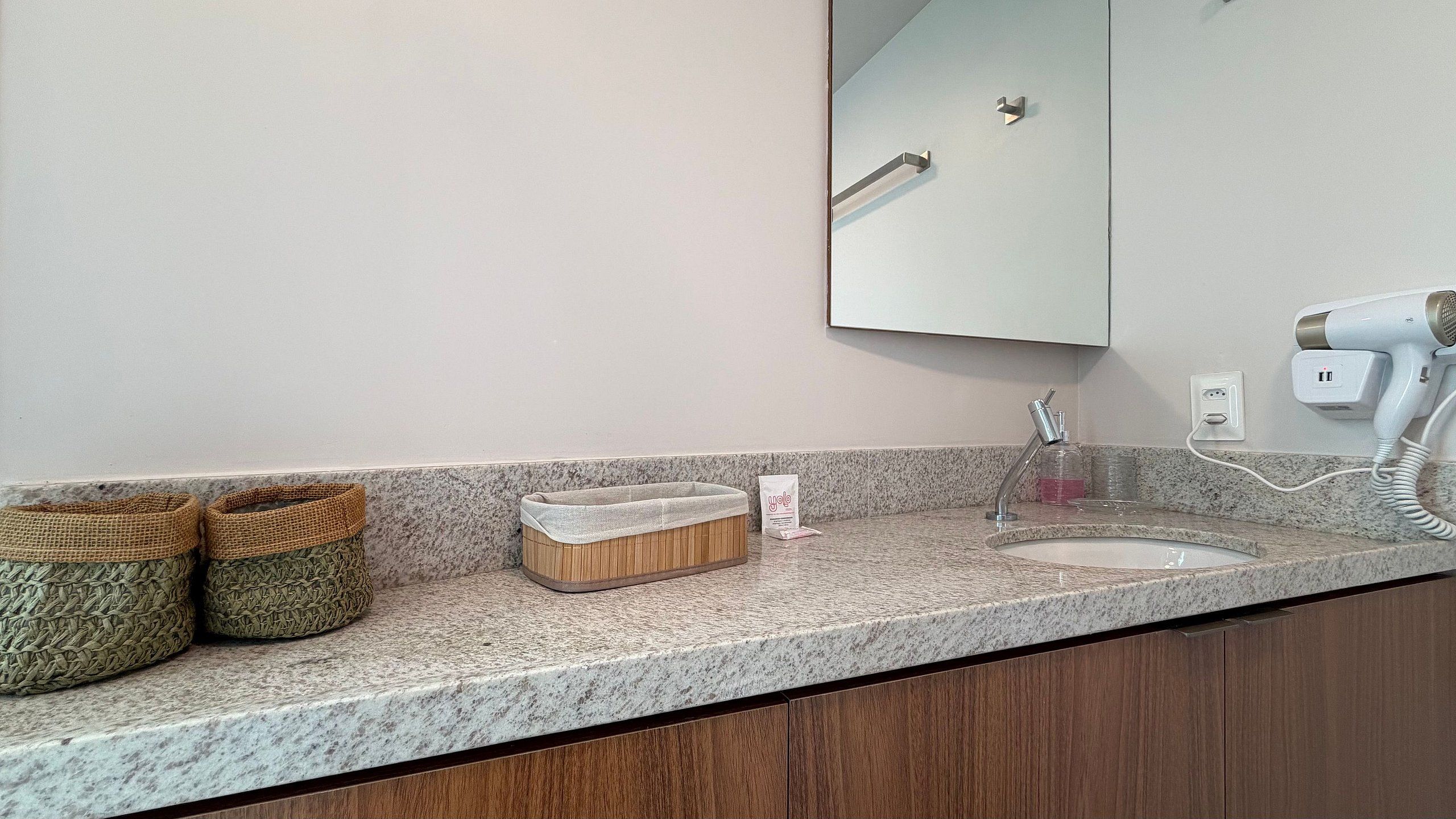 A bathroom with a granite countertop, a sink, a mirror, a towel dispenser, and two woven baskets.
