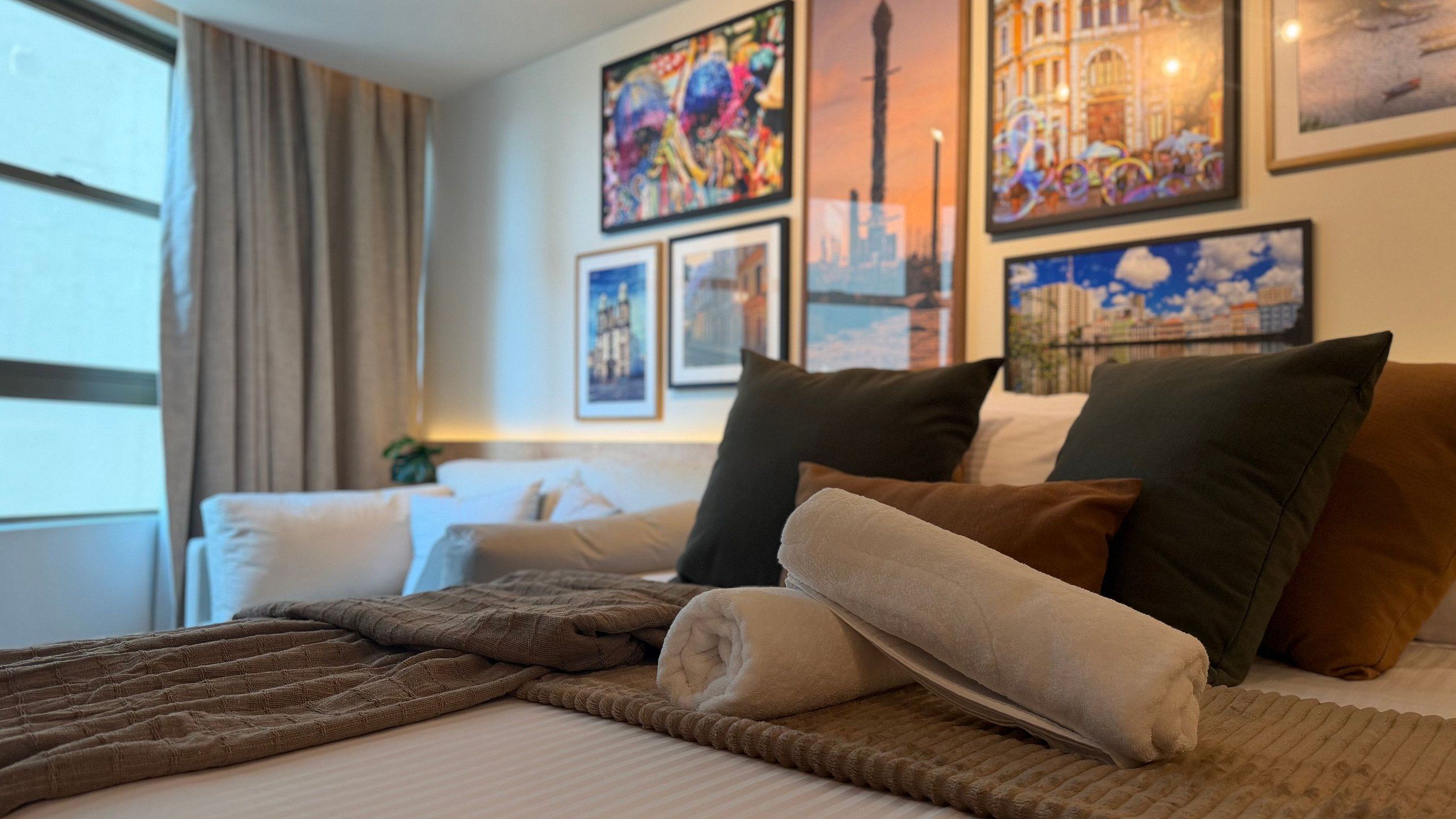 A hotel room with a bed, pillows, a blanket, and artwork on the wall.