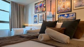 A hotel room with a bed, pillows, a blanket, and artwork on the wall.