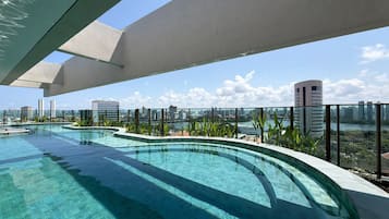 A rooftop infinity pool with a city view, surrounded by greenery and modern architecture.