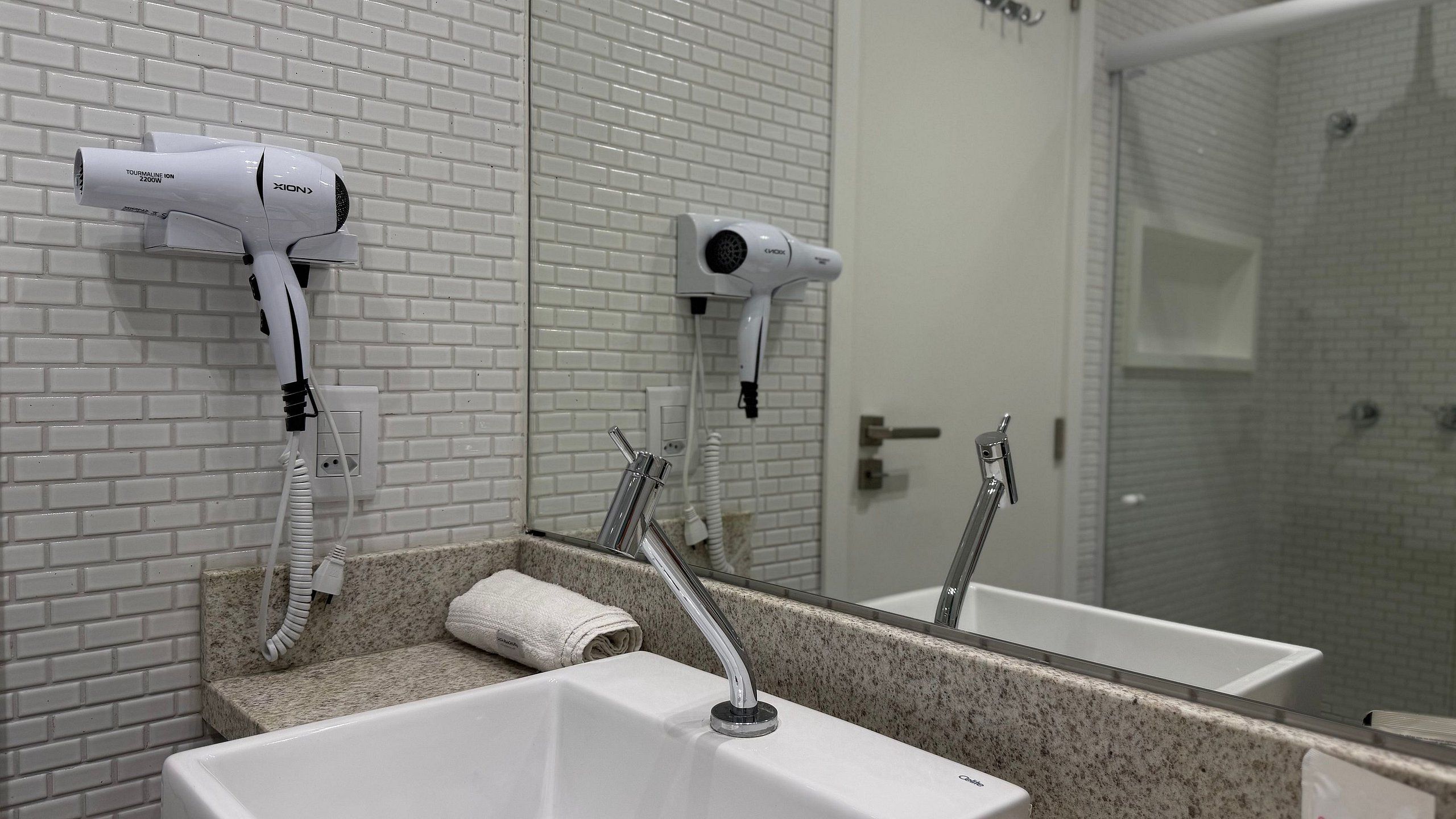 A bathroom with two hair dryers mounted on the wall, a sink with a towel, and a shower area.