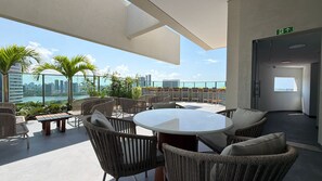 A rooftop lounge with wicker furniture, a round table, and a view of the city skyline.