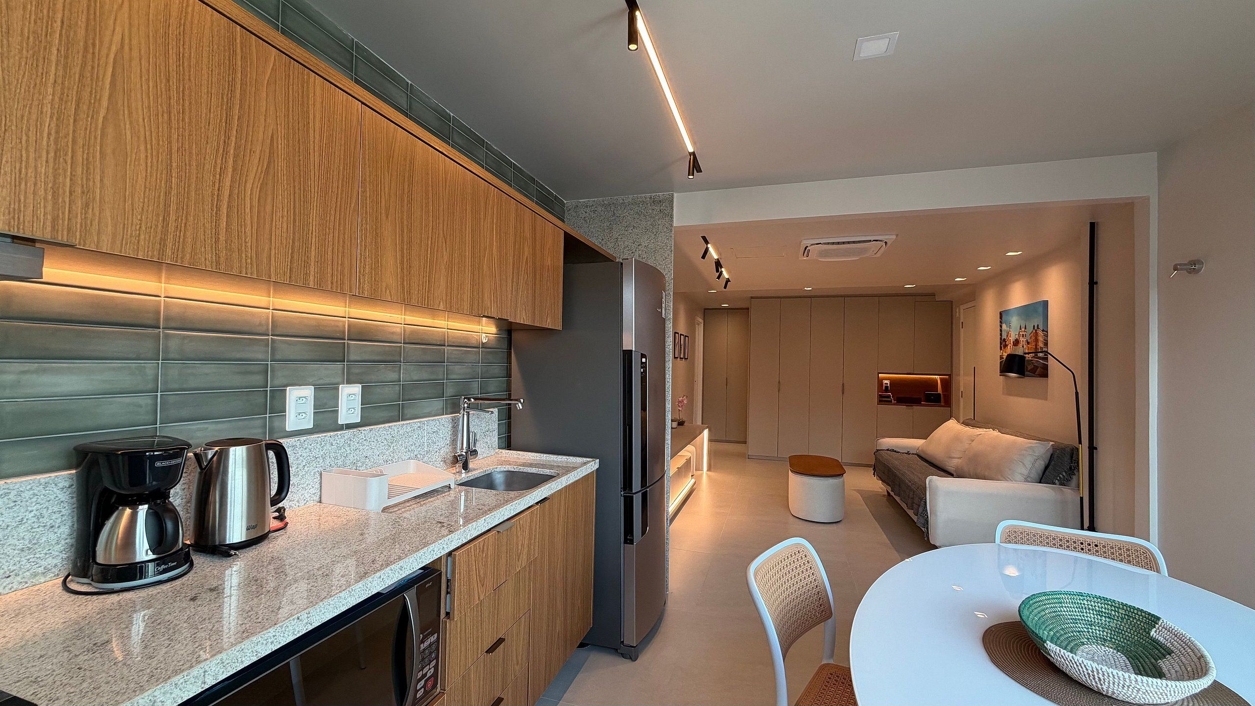 A modern kitchen with a coffee maker, a refrigerator, and a dining area with a table and chairs.