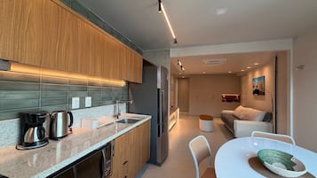 A modern kitchen with a coffee maker, a refrigerator, and a dining area with a table and chairs.