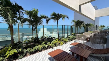 Une terrasse sur le toit offrant une vue sur l’océan, les palmiers et agrémentée de mobilier d’extérieur moderne.