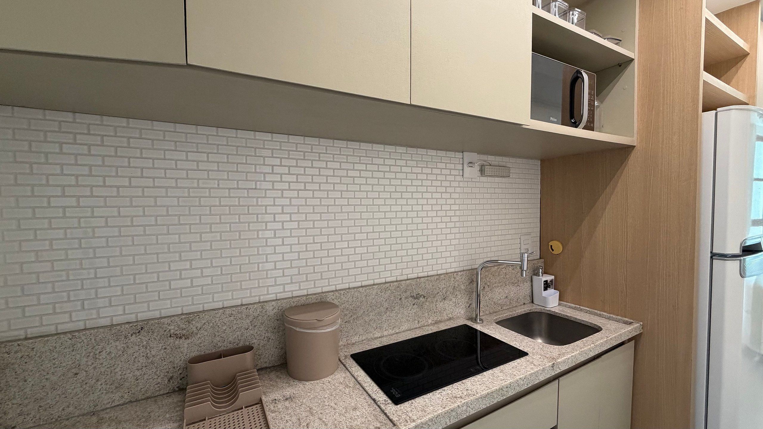Una cocina con baldosas blancas tipo metro, encimera de granito, pileta doble y refrigerador blanco.