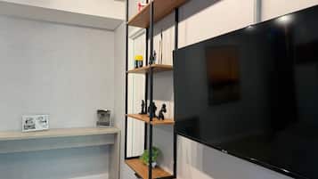 A modern living room with a large flat-screen TV mounted on the wall, wooden shelves with decorative items, and a framed picture on a lower shelf.