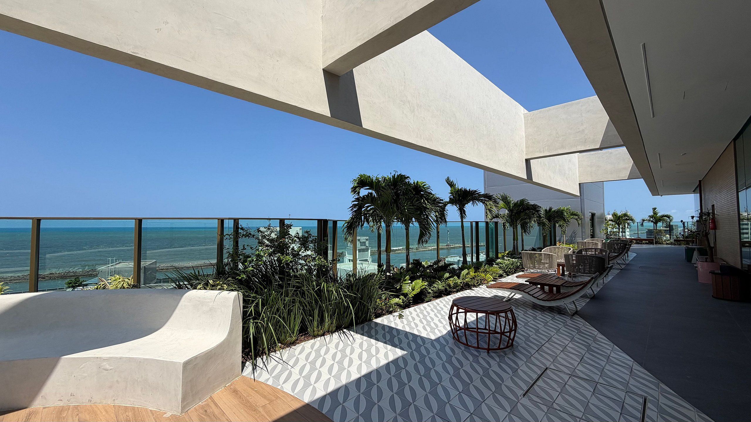 A modern outdoor seating area with a view of the ocean, featuring geometric patterns on the floor and contemporary furniture.