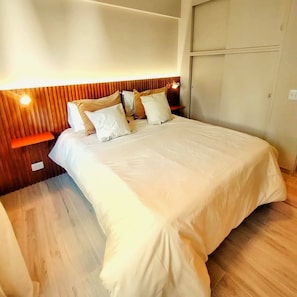 A bedroom with a bed, wooden headboard, bedside tables, and a wardrobe.