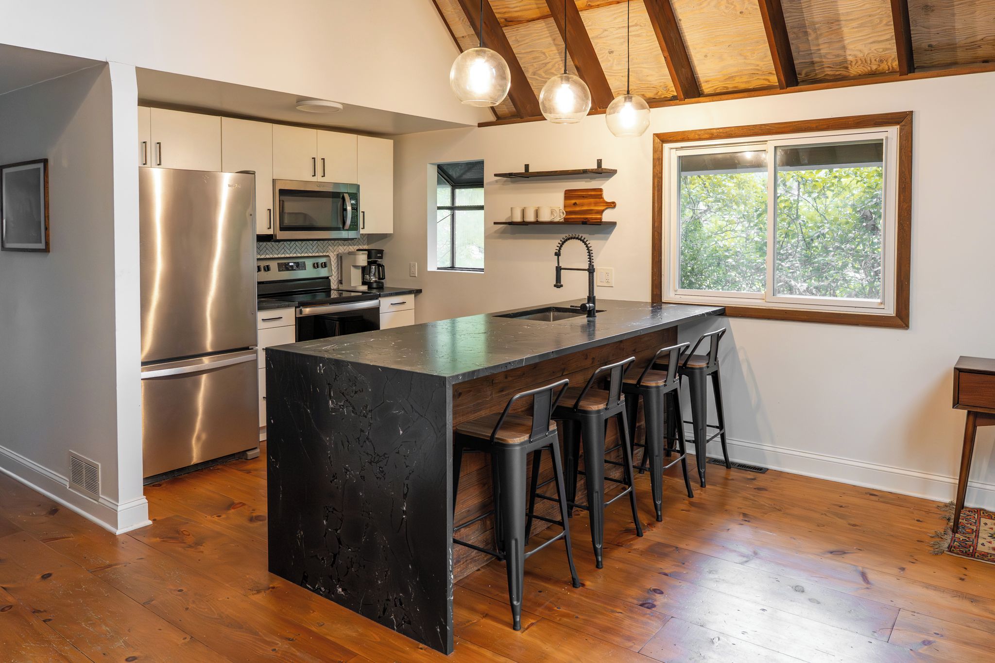 A kitchen with a central island, bar stools, stainless steel appliances, and a window with a view.