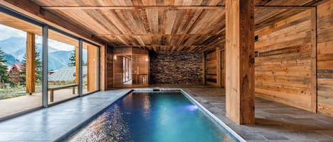 Une piscine intérieure moderne avec des poutres en bois au plafond et des murs en pierre.