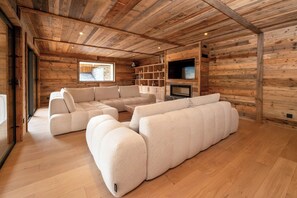 Interno di una baita in legno con un divano componibile, una TV a schermo piatto e scaffalature a muro.
