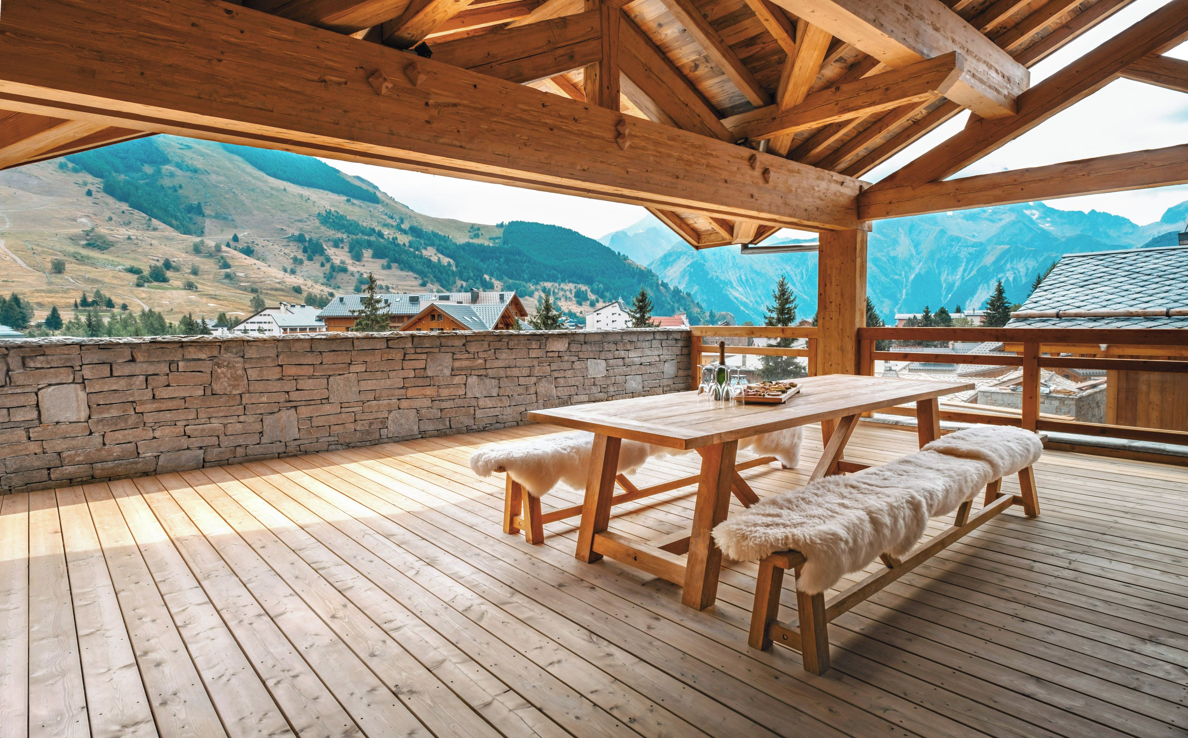 Eine Holzterrasse mit Tisch und Bänken, mit Blick auf eine gebirgige Landschaft.