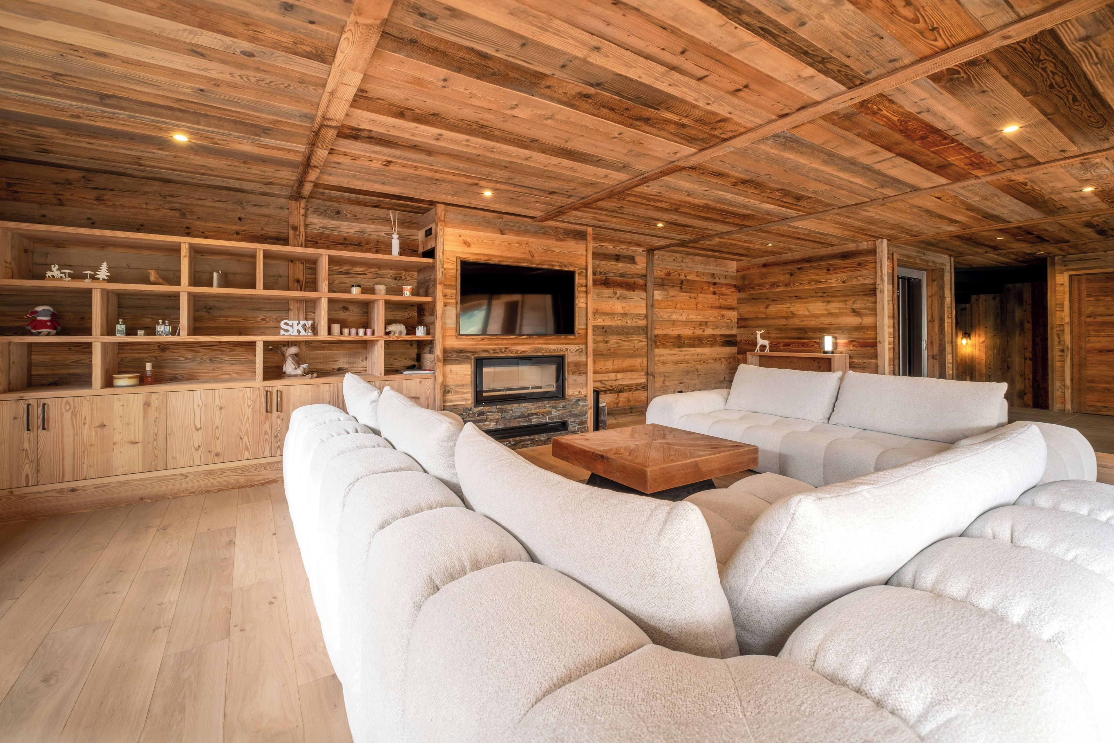 Una sala moderna con techo de madera, estanterías empotradas, chimenea y un amplio sofá modular.