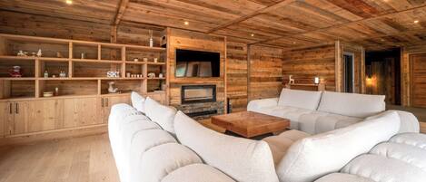 Una sala moderna con techo de madera, estanterías empotradas, chimenea y un amplio sofá modular.
