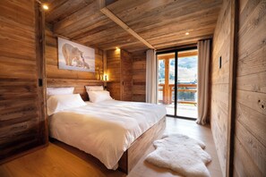 Une chambre à coucher dans une cabane en bois, avec un lit, un tableau représentant des ours polaires accroché au mur, et une vue sur un paysage montagneux par une porte vitrée.