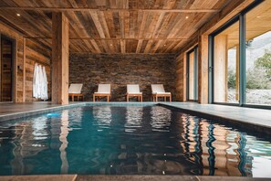 Ein Hallenbad mit Holzbalkendecke, Steinwand und vier Liegestühlen.