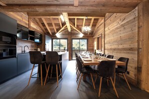 A modern kitchen with a dining area, wooden beams, and large windows. - Exceptional Chalet – Luxury & Mountain Views (Les Deux Alpes)