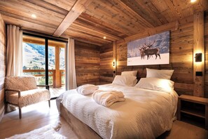 Ein schlichtes Schlafzimmer im Blockhausstil mit einem großen Bett, einem Sessel und einem Hirschgemälde an der Wand.