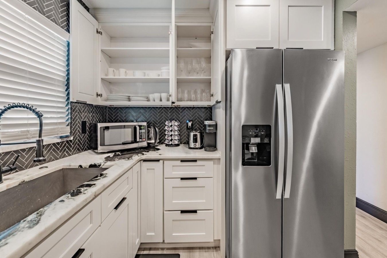A kitchen with white cabinets, a stainless steel refrigerator, a microwave, and a coffee maker.