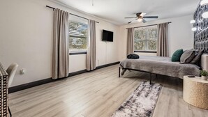 A modern bedroom with a bed, ceiling fans, a TV, and large windows. - Tampa Lake House – Dock, Pool Table & Putt Green (Tampa)