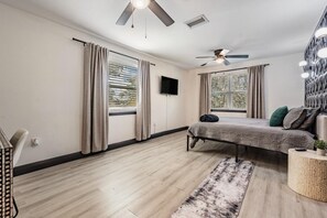 A modern bedroom with a bed, ceiling fans, a TV, and large windows.