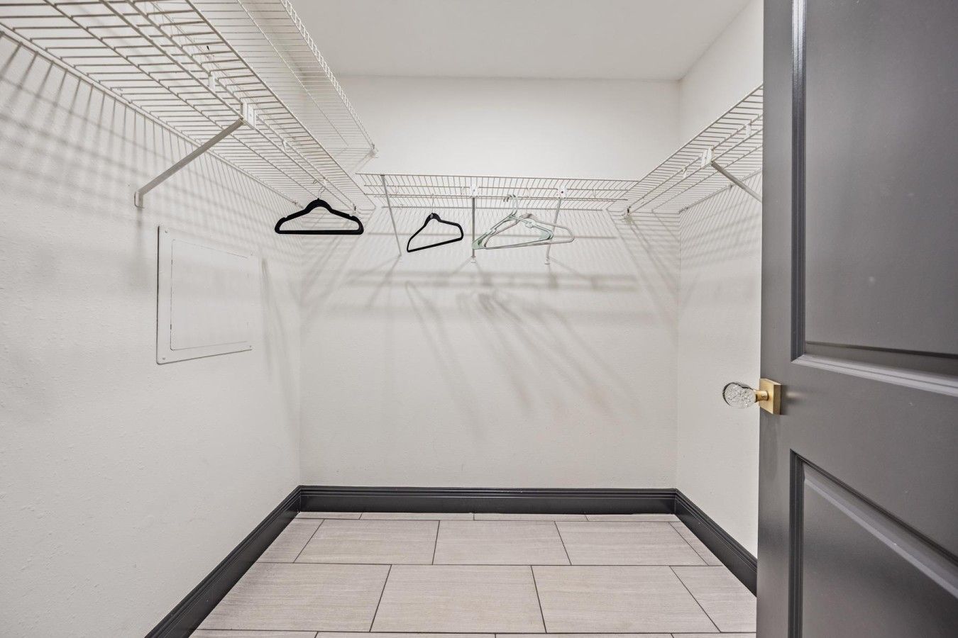 Una habitación con suelo de baldosas, una puerta a la derecha y un tendedero con perchas.