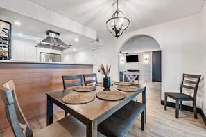 A modern dining area with a wooden table, woven placemats, and a chandelier.