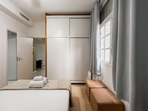 Ein Schlafzimmer mit einem Bett, einem Kleiderschrank, einer Bank und einem Fenster mit Vorhängen.