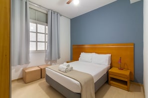Ein Schlafzimmer mit einem Bett, einem Nachttisch, einem Fenster mit Vorhängen und Holzboden.