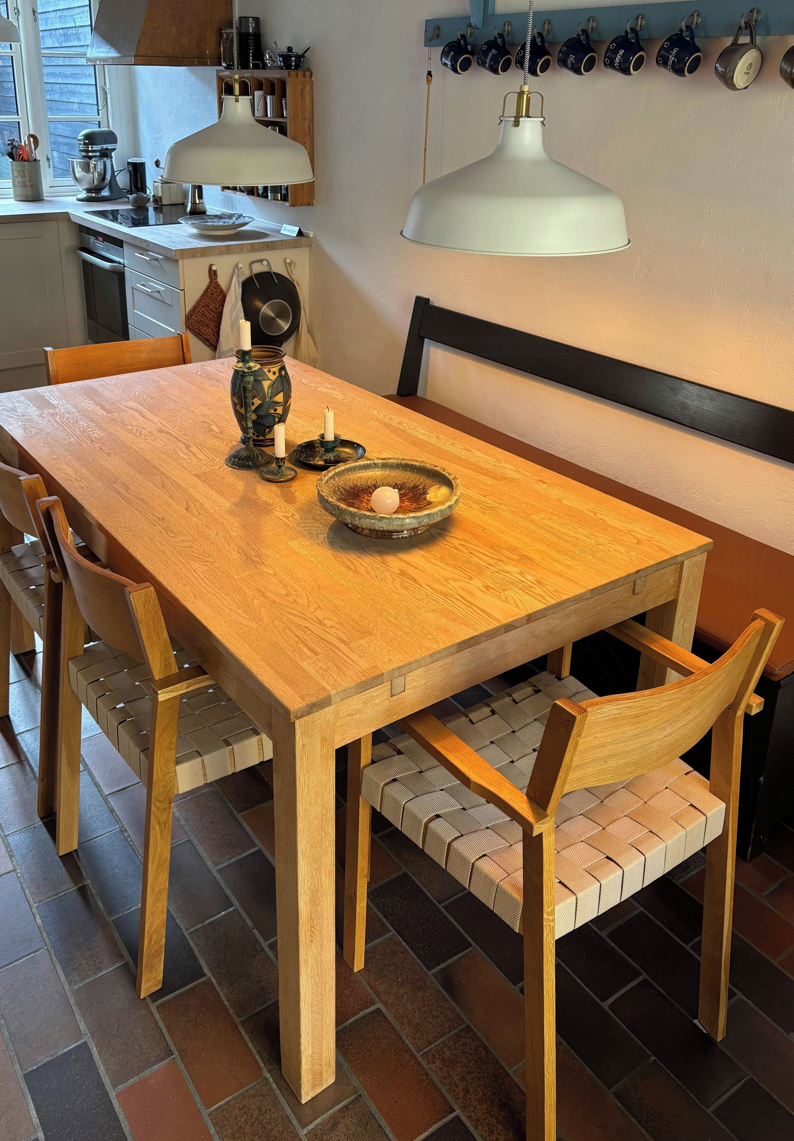 A wooden dining table with a bench, surrounded by chairs with woven seats.