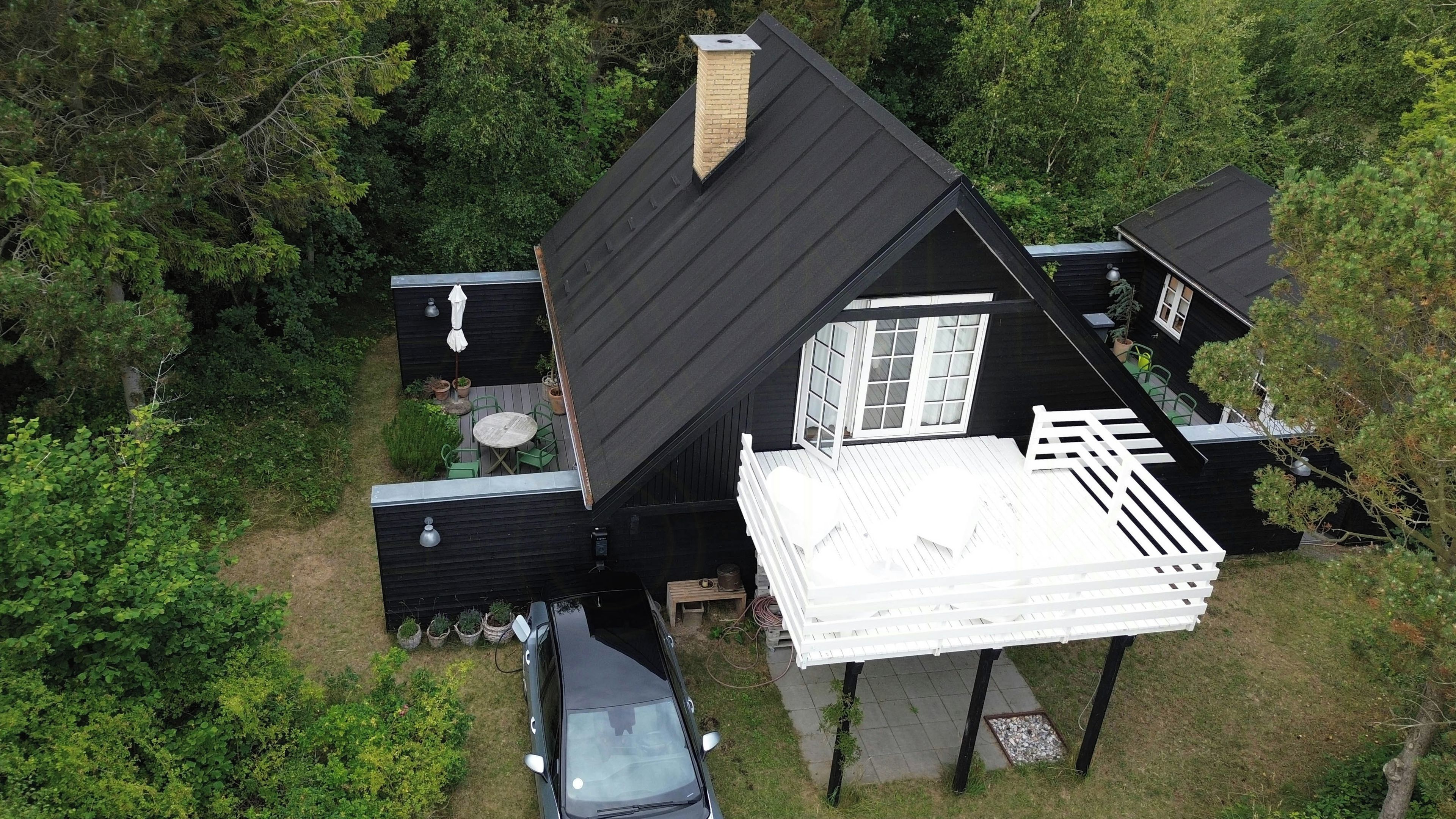 Une maison noire avec un balcon blanc, entourée de verdure.