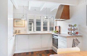 A kitchen with white cabinets, a wooden countertop, a hanging light fixture, and a window with blinds. - House decorated in a classic style, near the water (Ebeltoft)