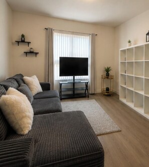 A living room with a sofa, TV, and a bookshelf. - Furnished 3BR Indio Apartment • 30+ Day Stays (Indio)
