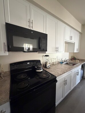 A kitchen with white cabinets, a black stove, a microwave, and a blender. - Furnished 3BR Indio Apartment • 30+ Day Stays (Indio)