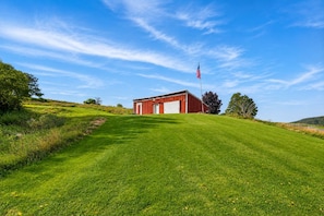 A red barn with a white door and an American flag on a grassy hill.
