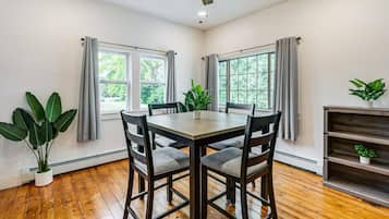 Un coin repas avec une table et des chaises en bois, de grandes fenêtres avec des rideaux et un ventilateur de plafond.