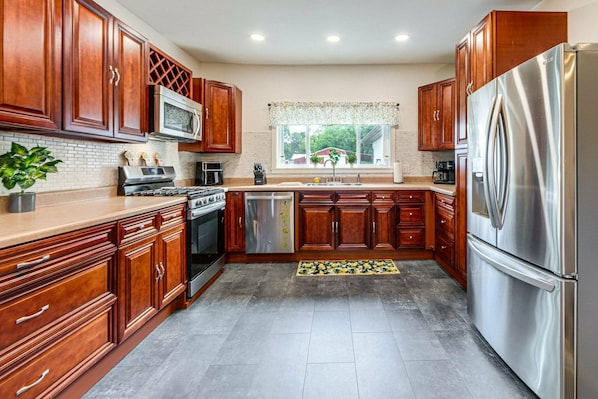 A kitchen with wooden cabinets, stainless steel appliances, a window with a view, and a tiled floor.