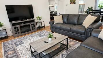 Un salon moderne avec un téléviseur à écran plat, un canapé en cuir, une table basse et un tapis à motifs.
