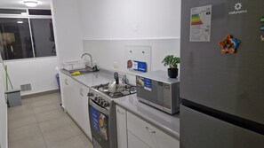 Une cuisine équipée d’une cuisinière, d’un four à micro-ondes, d’un réfrigérateur et d’une fenêtre avec des stores.