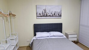 Une chambre d’hôtel avec un lit, une table de chevet, un porte-manteau fixé au mur et un tableau représentant un paysage urbain.