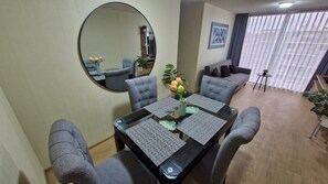 En matplats med en rund spegel, grå klädda stolar, ett glasbord med mönstrade bordstabletter och en vas med blommor.