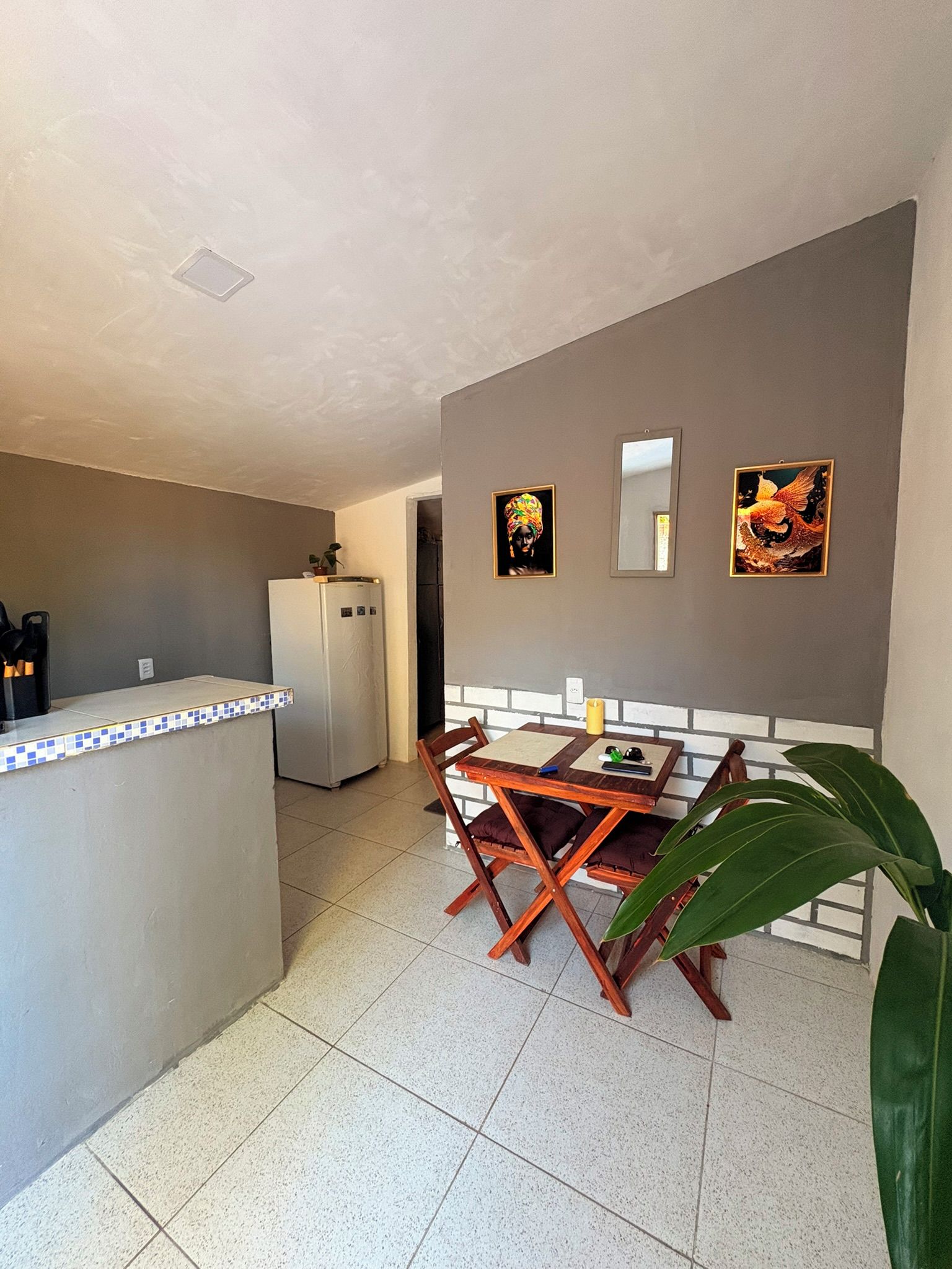 Cozinha compacta com geladeira, mesa de jantar com cadeiras e uma ilha pequena com bancada azulejada.