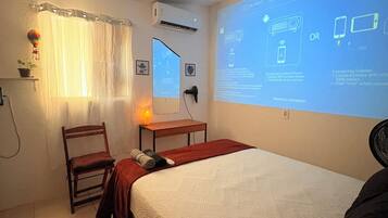 Quarto de hotel com uma cama, uma cadeira, uma escrivaninha e uma tela de projetor exibindo instruções.