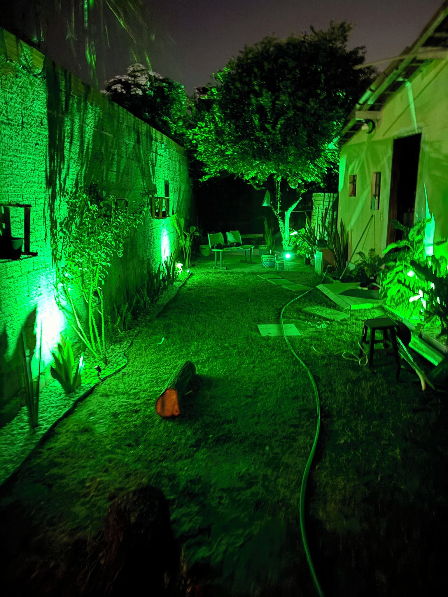 Área externa com pouca luz, um caminho, uma mesa pequena e uma estrutura parecida com uma tenda.