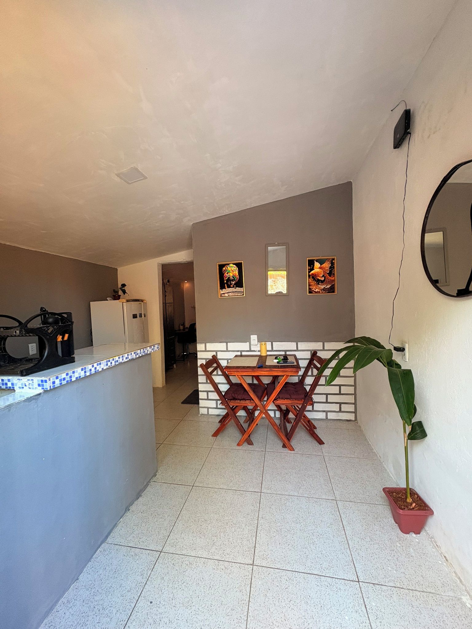 Cozinha compacta com área de refeições, geladeira, pia e um vaso de planta.